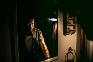 man standing in front of a mirror in the grips of a strong emotion