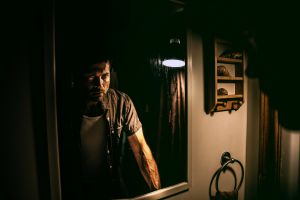 man standing in front of a mirror in the grips of a strong emotion