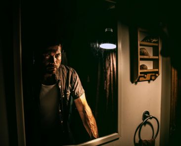 man standing in front of a mirror in the grips of a strong emotion