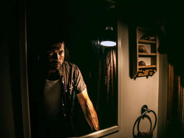 man standing in front of a mirror in the grips of a strong emotion